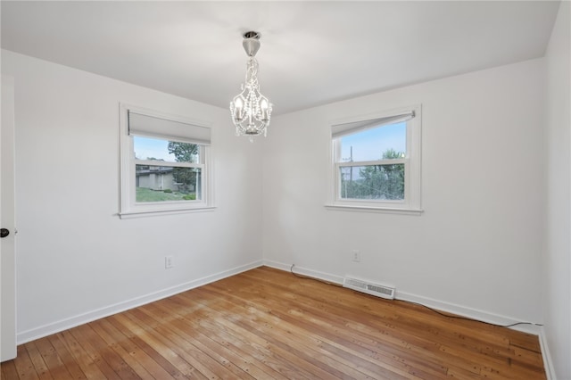 unfurnished room with a healthy amount of sunlight, a notable chandelier, and wood-type flooring