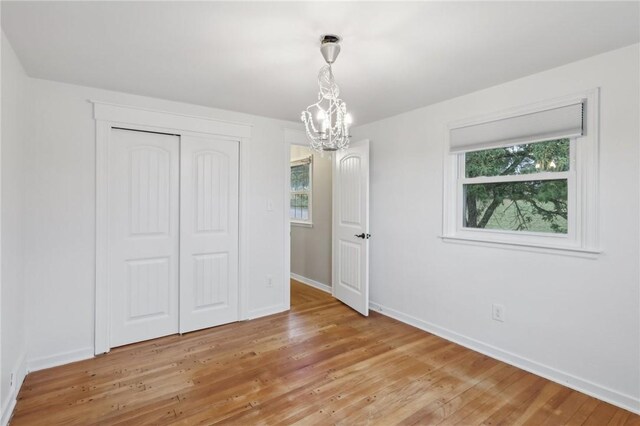 unfurnished bedroom featuring a notable chandelier, a closet, multiple windows, and light hardwood / wood-style floors