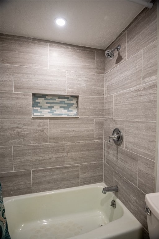 bathroom featuring toilet, tiled shower / bath combo, and a textured ceiling