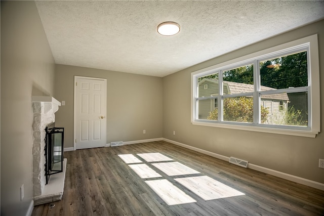 unfurnished living room featuring hardwood / wood-style flooring, a textured ceiling, and a stone fireplace