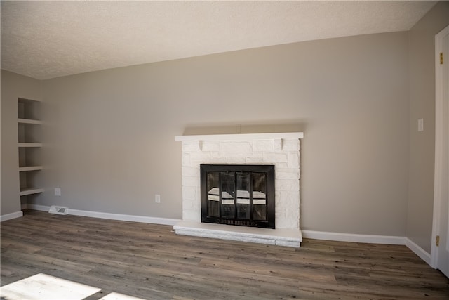 unfurnished living room with a textured ceiling, hardwood / wood-style flooring, built in shelves, and a stone fireplace