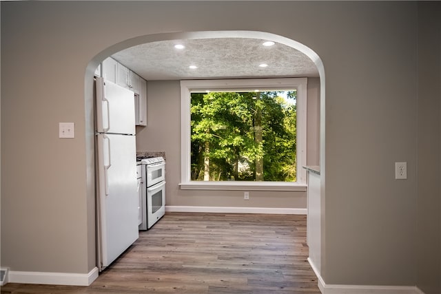 kitchen featuring a textured ceiling, light hardwood / wood-style flooring, a healthy amount of sunlight, and white appliances