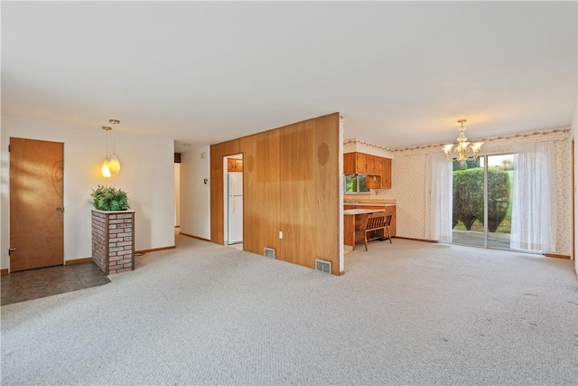 unfurnished living room with wood walls, light carpet, and an inviting chandelier