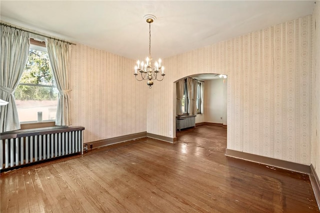 empty room featuring radiator heating unit, a notable chandelier, and hardwood / wood-style floors