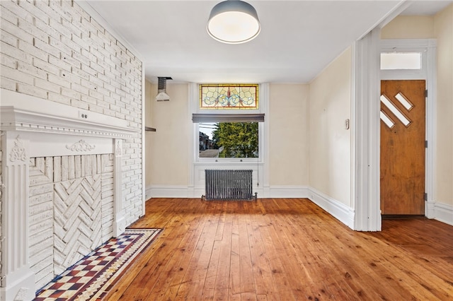 unfurnished living room featuring radiator, a brick fireplace, and hardwood / wood-style flooring