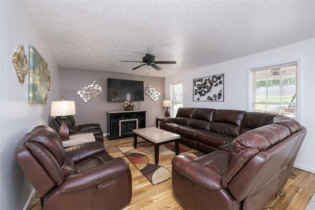 living room featuring a fireplace, a textured ceiling, light wood-type flooring, and ceiling fan