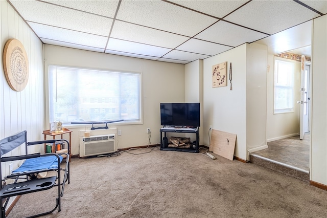 carpeted living room featuring a paneled ceiling, wood walls, and an AC wall unit