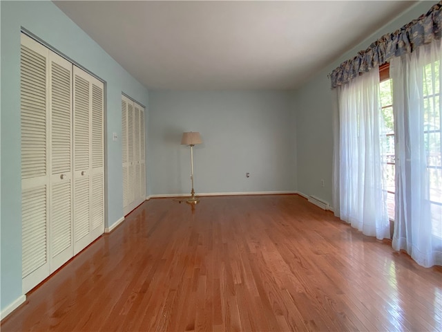 unfurnished bedroom with multiple closets, hardwood / wood-style floors, and a baseboard radiator