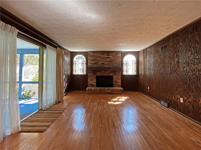 unfurnished living room with wood-type flooring, plenty of natural light, and a brick fireplace