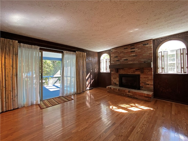 unfurnished living room featuring a textured ceiling, a brick fireplace, wood-type flooring, and wood walls