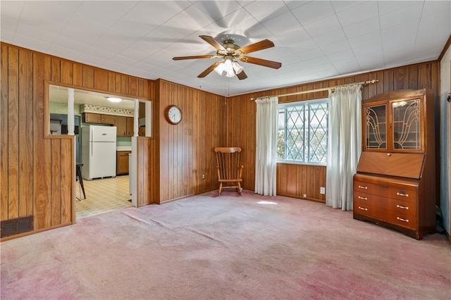 unfurnished bedroom with white fridge, wooden walls, light carpet, and ceiling fan