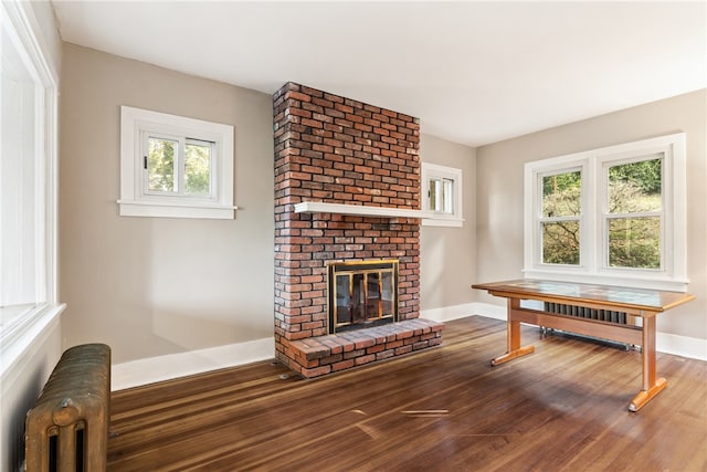 living room featuring plenty of natural light, dark hardwood / wood-style floors, radiator heating unit, and a brick fireplace