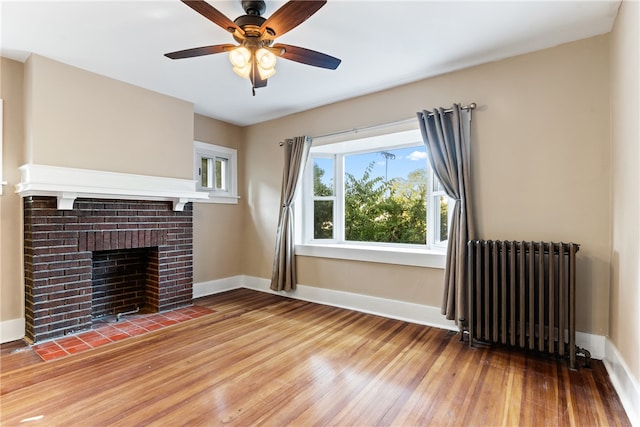 unfurnished living room featuring a fireplace, radiator, wood-type flooring, and ceiling fan