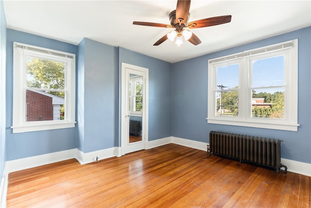 unfurnished room with hardwood / wood-style floors, ceiling fan, radiator heating unit, and a healthy amount of sunlight