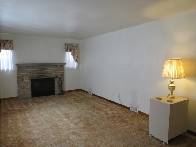 unfurnished living room featuring a stone fireplace, carpet flooring, and plenty of natural light