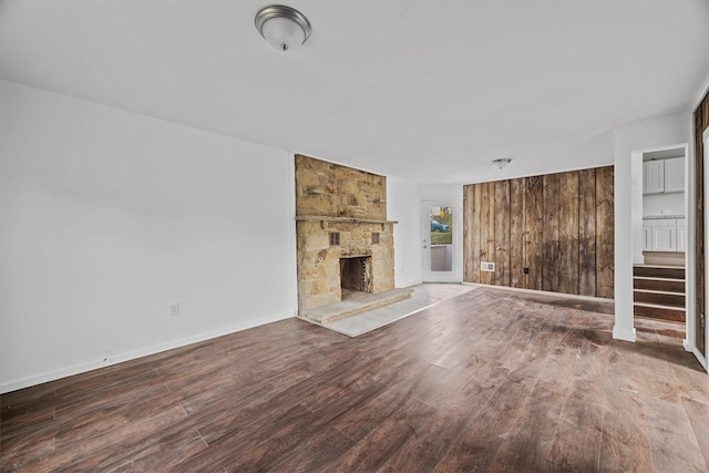 unfurnished living room with a fireplace, hardwood / wood-style floors, and wooden walls