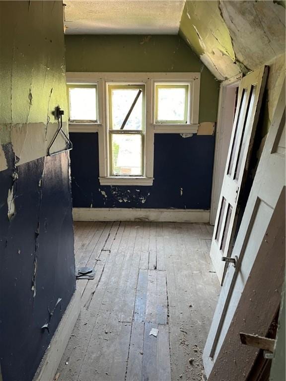 additional living space with light wood-style flooring, a textured ceiling, baseboards, and lofted ceiling