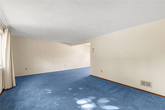 carpeted empty room featuring wood walls