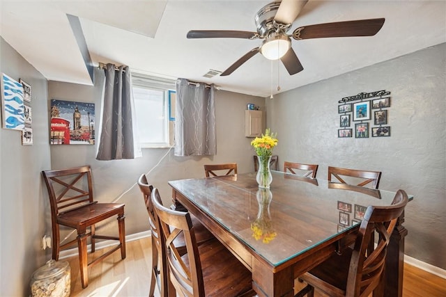 dining room with visible vents, a ceiling fan, light wood finished floors, baseboards, and a textured wall