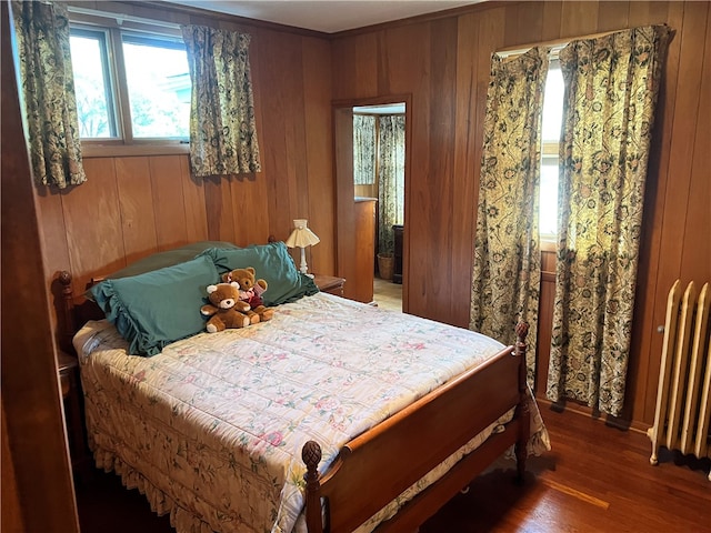 bedroom featuring wooden walls, radiator heating unit, and dark hardwood / wood-style floors