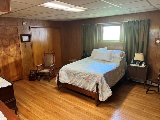 bedroom with wooden walls, light hardwood / wood-style flooring, and a paneled ceiling