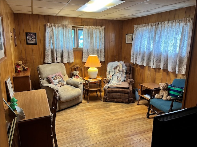 living area with a drop ceiling, light hardwood / wood-style flooring, and wooden walls