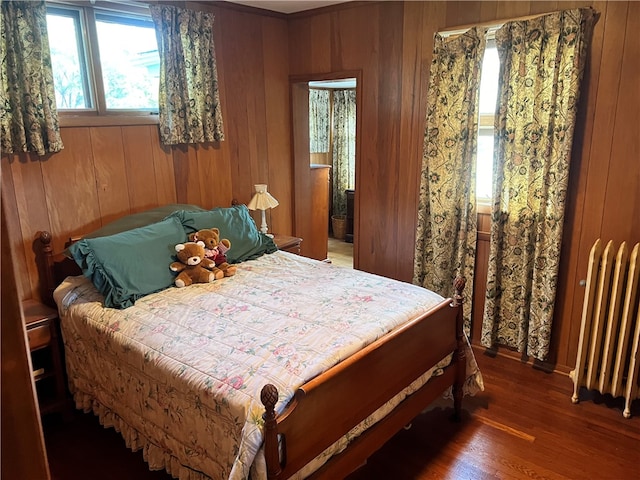 bedroom featuring dark hardwood / wood-style floors, wood walls, and radiator heating unit