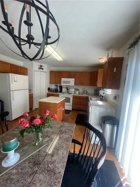 kitchen featuring white appliances, wood-type flooring, a kitchen island, an inviting chandelier, and sink