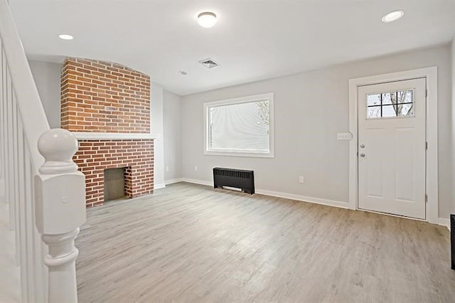 unfurnished living room with radiator, a brick fireplace, and light hardwood / wood-style floors