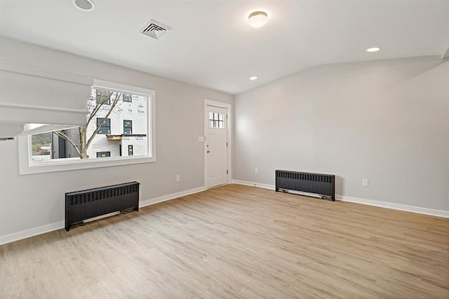 unfurnished living room with light hardwood / wood-style floors, radiator heating unit, and vaulted ceiling