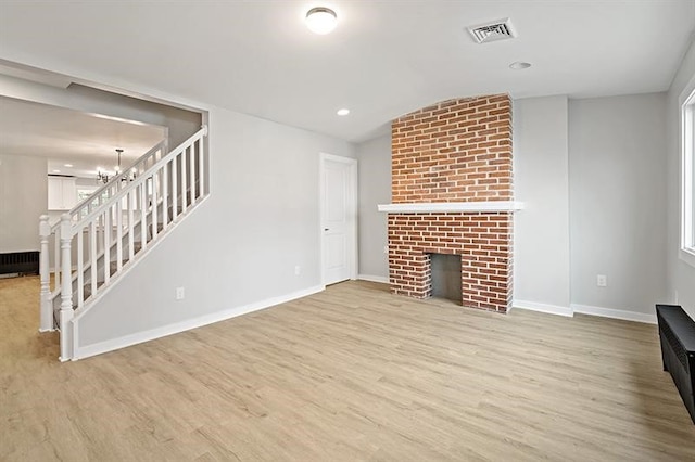 unfurnished living room featuring light hardwood / wood-style floors, plenty of natural light, an inviting chandelier, and a brick fireplace