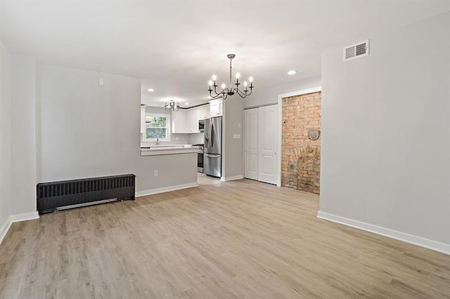 unfurnished living room with light wood-type flooring, radiator, and a notable chandelier