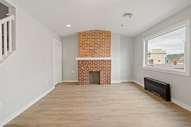 unfurnished living room with light wood-type flooring, radiator, vaulted ceiling, and a brick fireplace