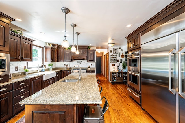 kitchen with a center island with sink, built in appliances, sink, and light hardwood / wood-style flooring