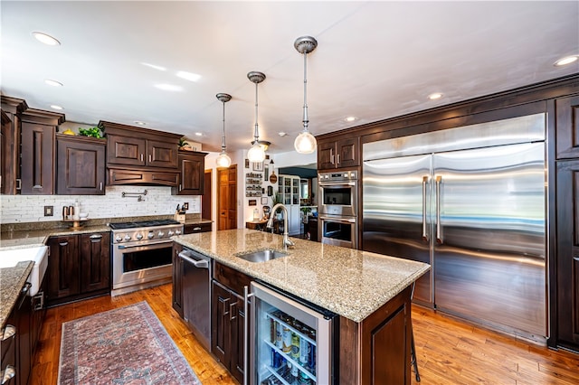 kitchen featuring light hardwood / wood-style flooring, beverage cooler, an island with sink, sink, and premium appliances