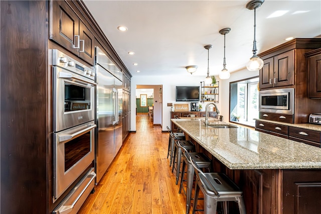 kitchen featuring built in appliances, a breakfast bar area, light hardwood / wood-style flooring, a kitchen island with sink, and sink