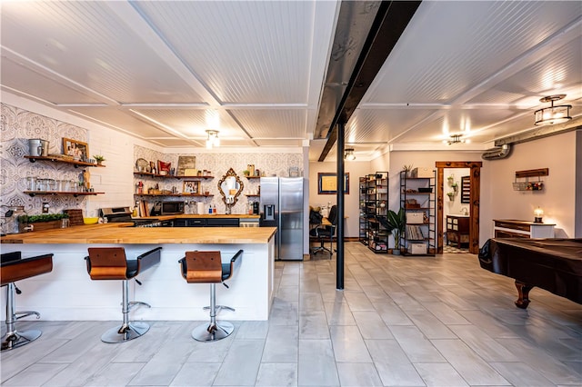 kitchen with billiards, butcher block countertops, kitchen peninsula, a breakfast bar, and appliances with stainless steel finishes