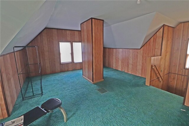 bonus room with lofted ceiling, wood walls, and dark colored carpet