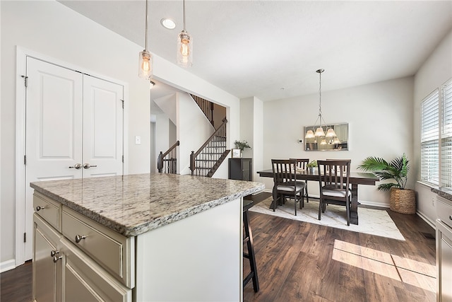 kitchen with a kitchen breakfast bar, a kitchen island, light stone countertops, hanging light fixtures, and dark hardwood / wood-style floors