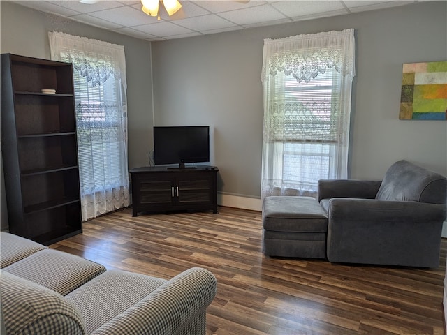 living room with a drop ceiling, dark wood-type flooring, and a wealth of natural light