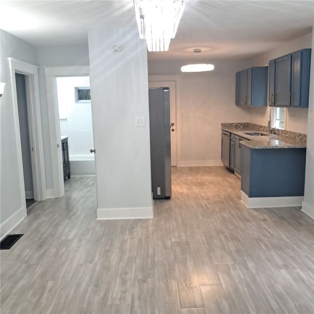 kitchen with light wood-type flooring, dark stone counters, stainless steel refrigerator, and sink