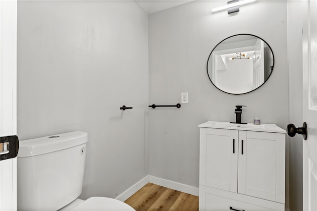 half bathroom featuring toilet, vanity, baseboards, and wood finished floors