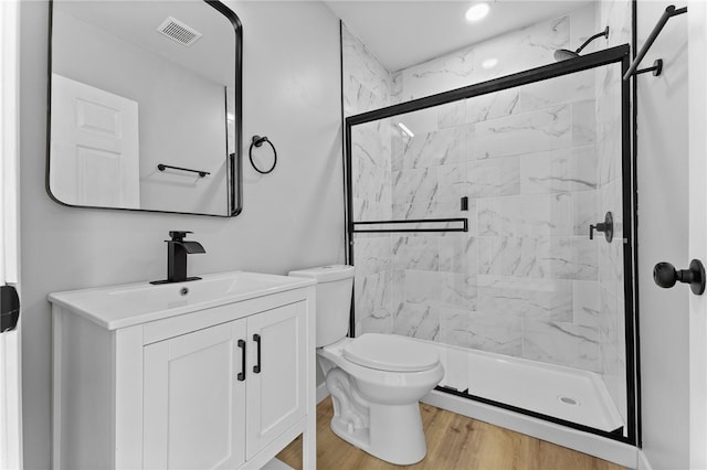 bathroom featuring a marble finish shower, visible vents, toilet, wood finished floors, and vanity