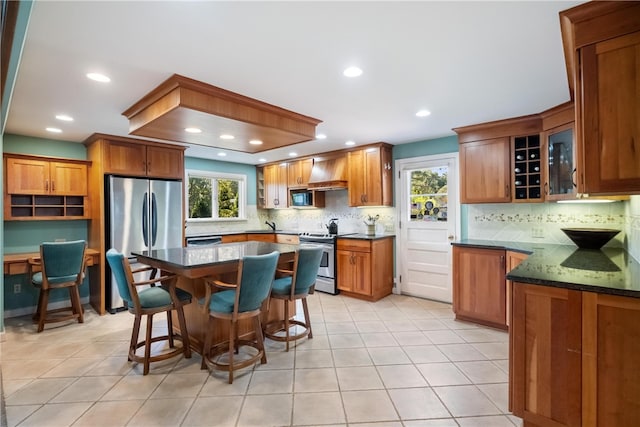 kitchen with tasteful backsplash, dark stone counters, a kitchen breakfast bar, custom range hood, and stainless steel appliances