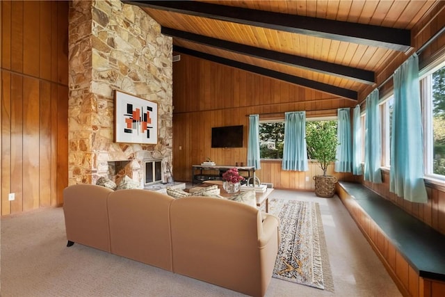 carpeted living room with wooden walls, a stone fireplace, vaulted ceiling with beams, and wood ceiling