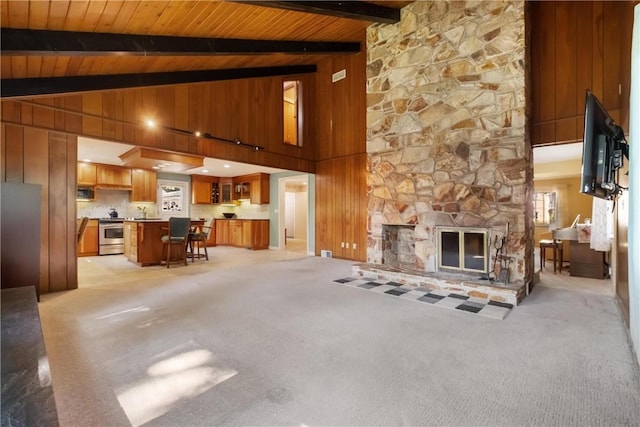 living area with wooden ceiling, a stone fireplace, beam ceiling, and light colored carpet