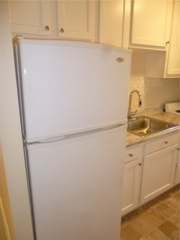 kitchen featuring white refrigerator, backsplash, sink, and white cabinets