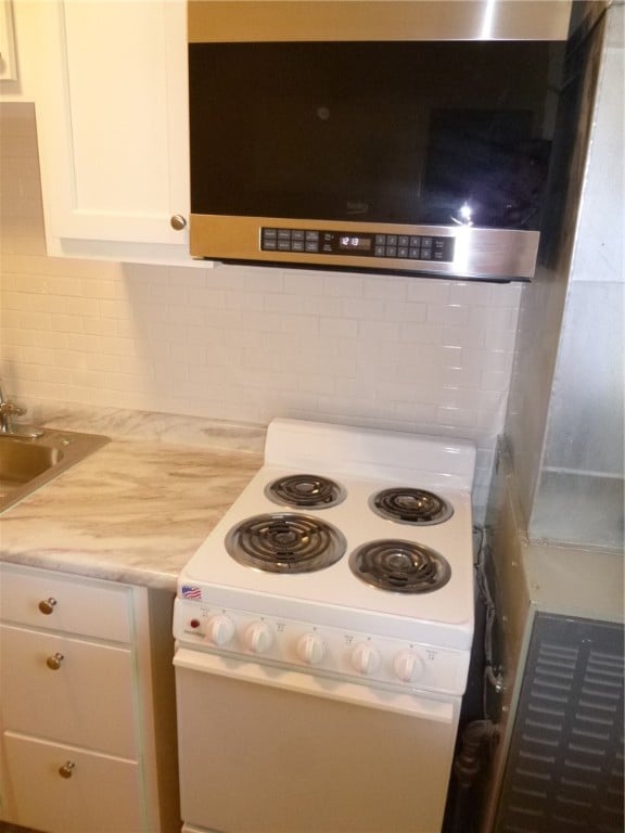 kitchen with electric range, decorative backsplash, white cabinetry, and sink