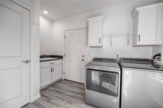 laundry room featuring separate washer and dryer, cabinets, sink, and light hardwood / wood-style floors