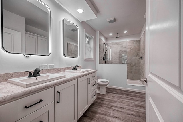 bathroom with tiled shower, wood-type flooring, toilet, and vanity